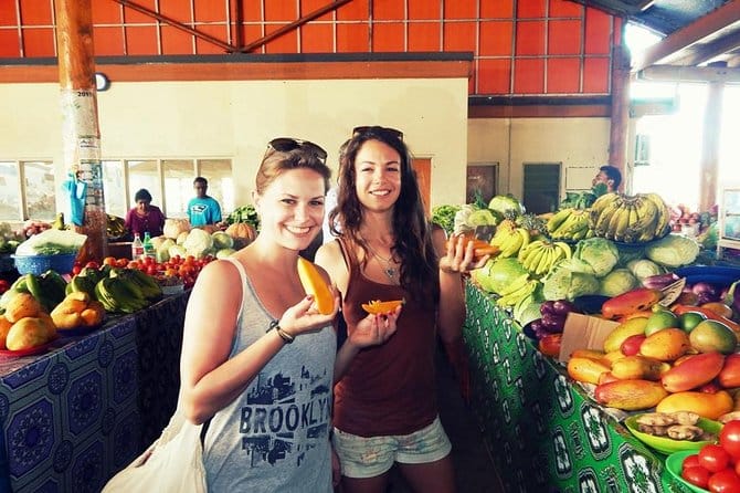 Two women smile while eating and buying fruits