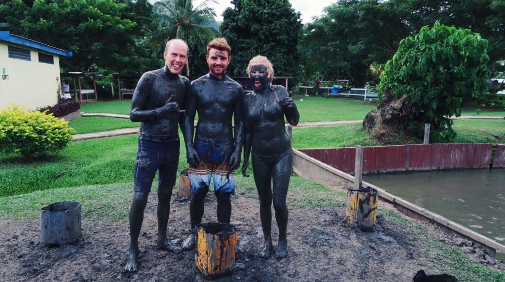 Two men and one woman smiles in front of the camera with mud in the body