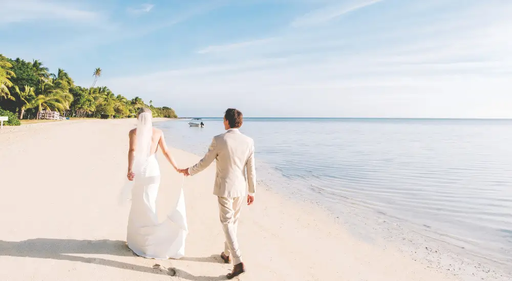 Married couple walk along a Fijian beach.