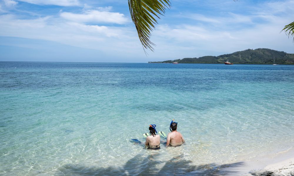 Couple in snorkelling gear sitting together in the shallow water of a turquoise Fiji lagoon