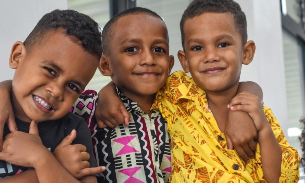 Three local children from Solevu Shell Village hugging and smiling