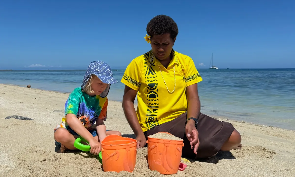 Child playing with a babysitter on a sandy beach.
