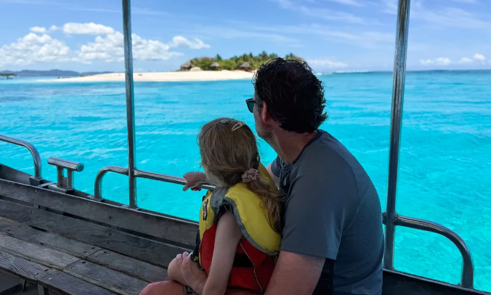 Father and child on a boat looking at a tropical island